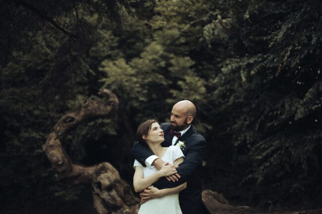 Les mariés enlacés dans un jardin, au pied d’un arbre tortueux, lors de leur mariage dans une maison familiale en Isère