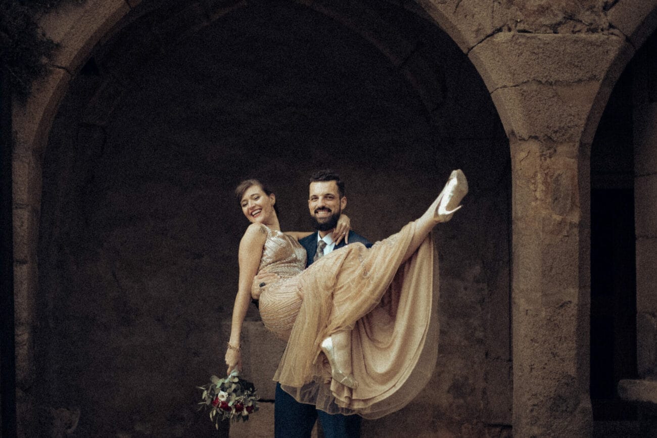 Photographe mariage Lyon – Marié portant sa femme en robe dorée dans une arche en pierre