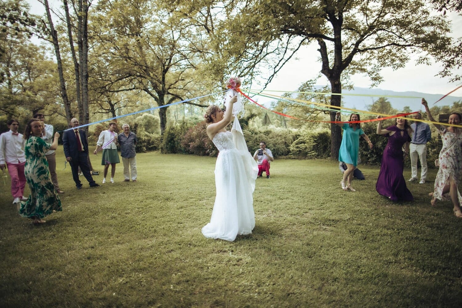 Une mariée tirant des rubans tenus par ses invitées, autour d’un bouquet suspendu.