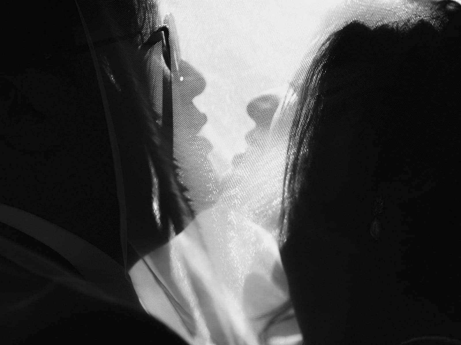 Photo artistique de mariage – silhouettes de mariés à travers un voile, jeu de lumière en noir et blanc