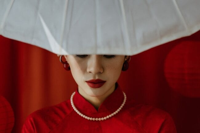 Vietnamese bride in traditional red áo dài with pearl necklace and white hat, during a wedding in Ho Chi Minh City