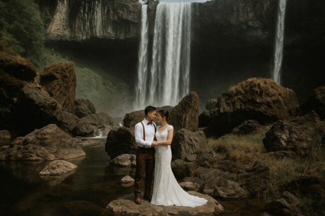 Bride and groom standing in front of waterfalls during an elopement or pre-wedding session in Vietnam’s highlands.