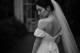 Elegant bride in off-shoulder wedding dress with long veil, in black and white portrait