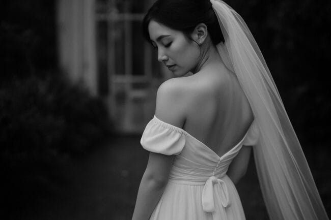 Elegant bride in off-shoulder wedding dress with long veil, in black and white portrait