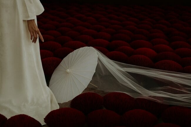 Bride in white áo dài with traditional paper umbrella and veil placed over red incense bundles in Vietnam