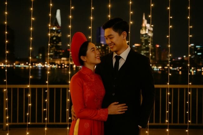 Vietnamese couple in traditional áo dài and suit during a night pre-wedding shoot in Ho Chi Minh City with skyline and fairy lights