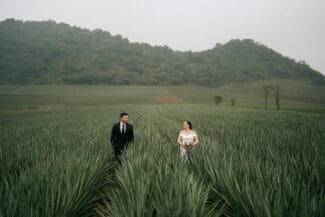 Bride and groom walking through a green field in Vietnam with hills in the background – outdoor wedding session