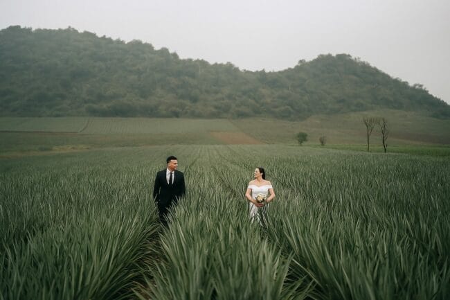 Bride and groom walking through a green field in Vietnam with hills in the background – outdoor wedding session