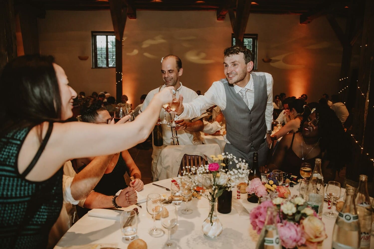 Le marié trinque avec les invités autour d’une table fleurie pendant le repas de mariage au Château de Pizay