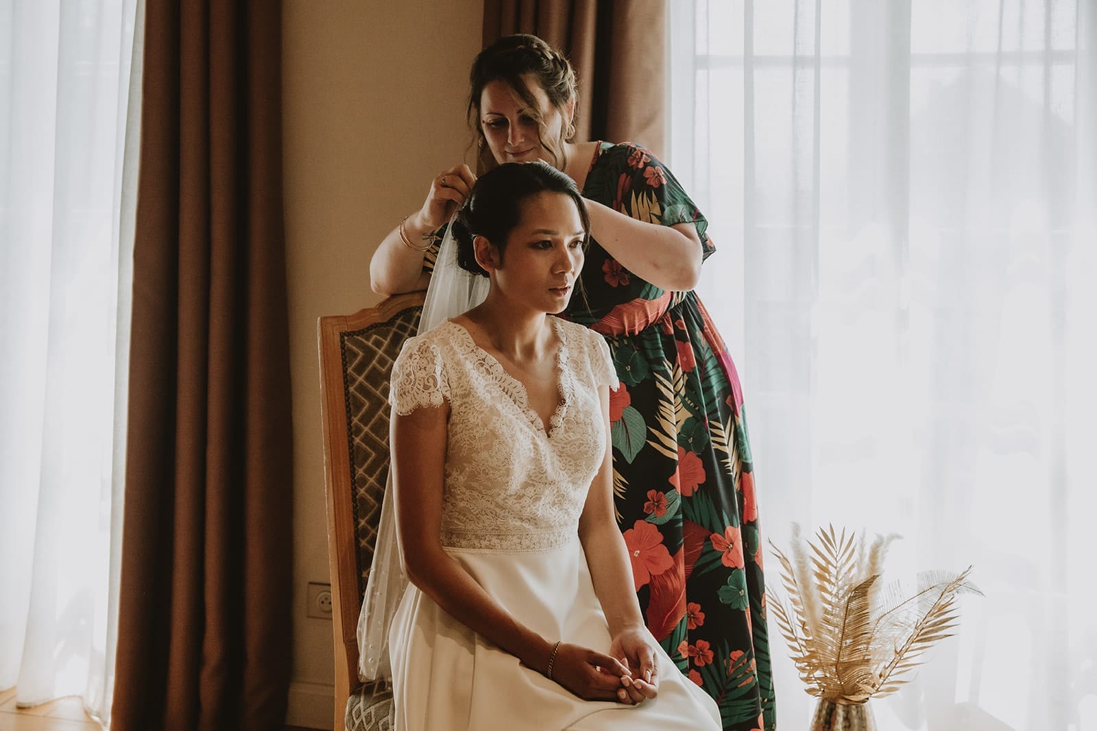 Une amie aide la mariée à ajuster son voile dans une chambre baignée de lumière au Château de Pizay, avant la cérémonie