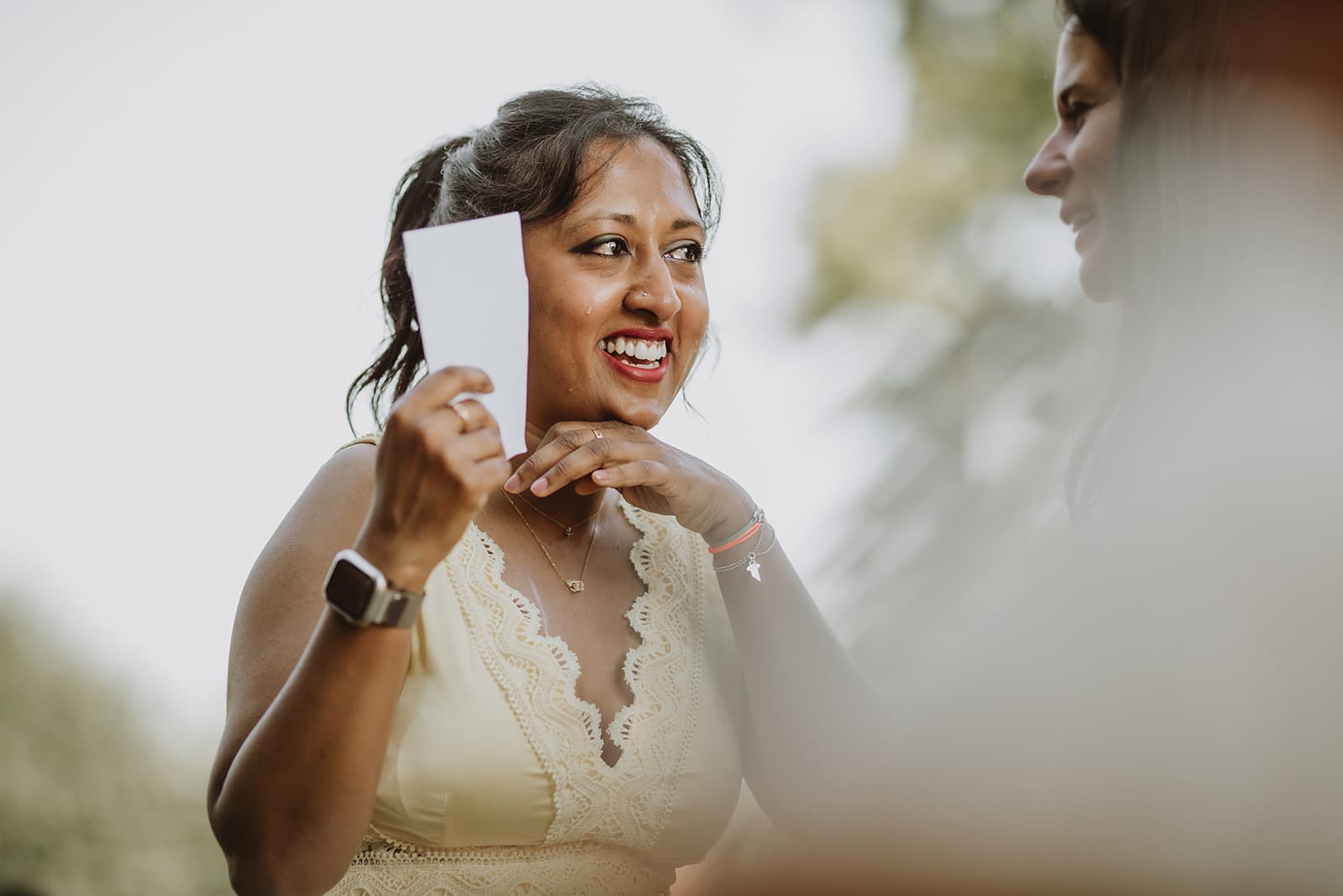 Une invitée éclate de rire tout en pleurant en tenant une carte, moment de complicité durant la cérémonie de mariage au Château de Pizay