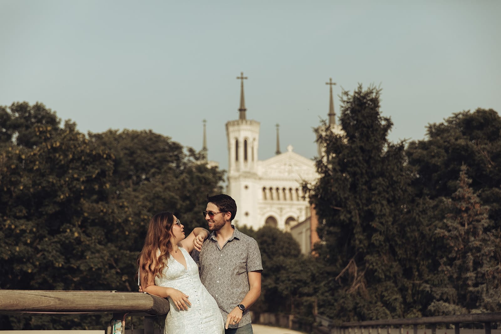 Couple souriant sur la passerelle des Quatre Vents à Lyon avec la basilique de Fourvière en arrière-plan
