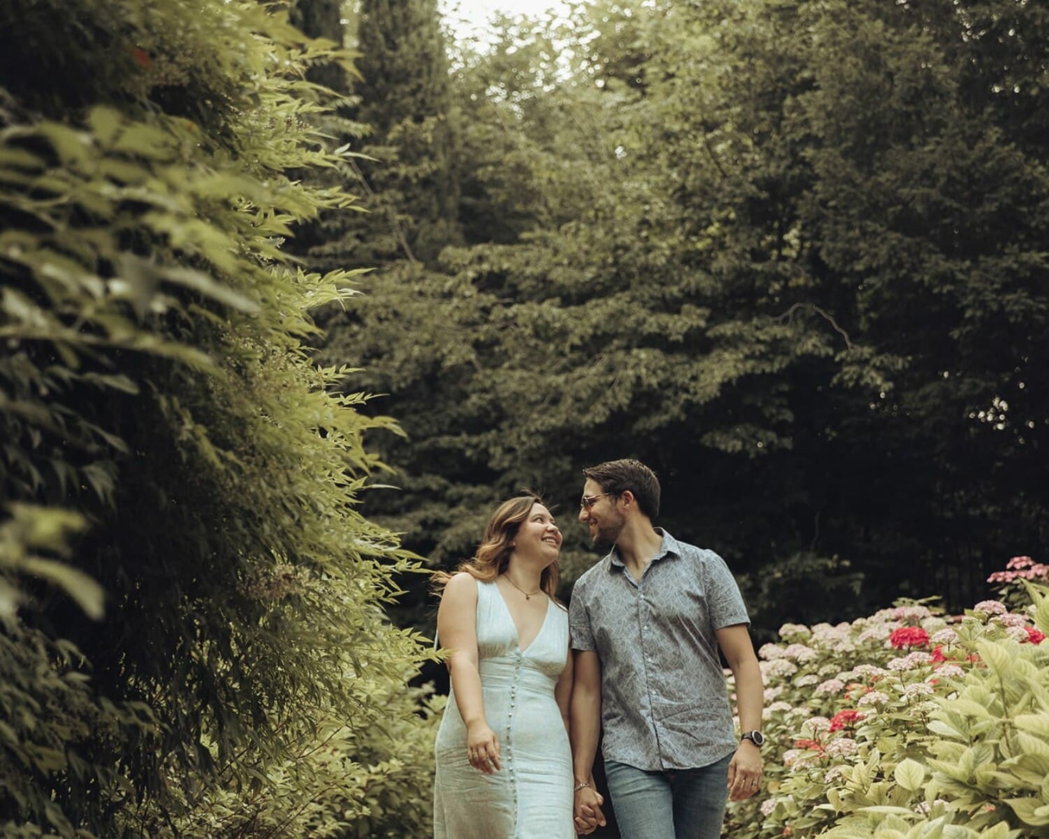 Couple marchant main dans la main dans un jardin fleuri, entouré de verdure