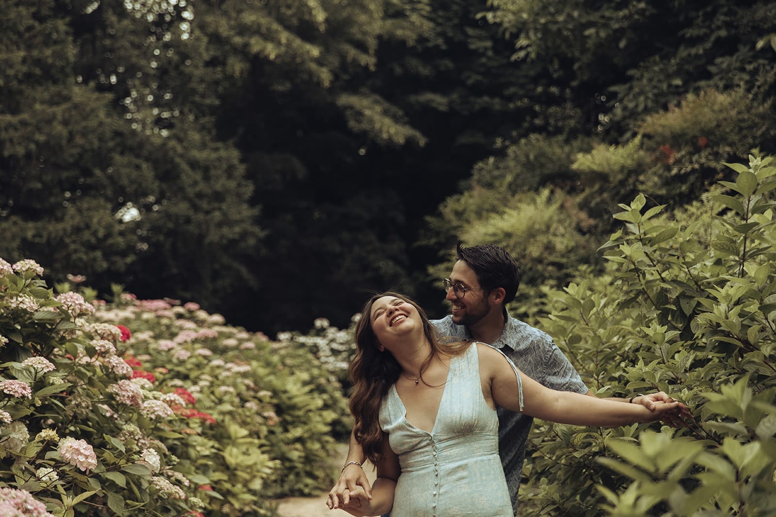 Femme riant aux éclats dans les bras de son partenaire, au cœur d’un jardin fleuri
