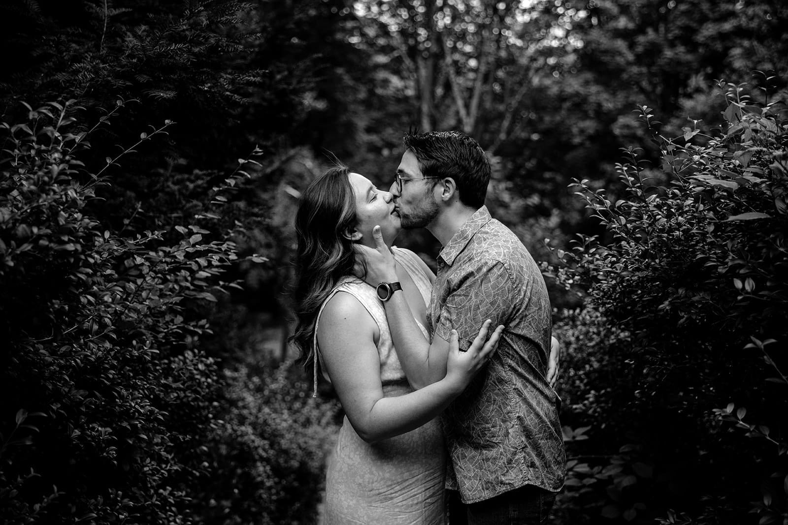Couple s’embrassant tendrement dans un jardin, en noir et blanc, au milieu de la végétation
