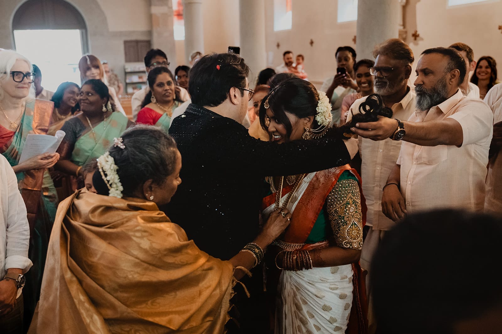 Moment fort du mariage : le marié attache le collier sacré autour du cou de la mariée, entouré par les familles et les chants