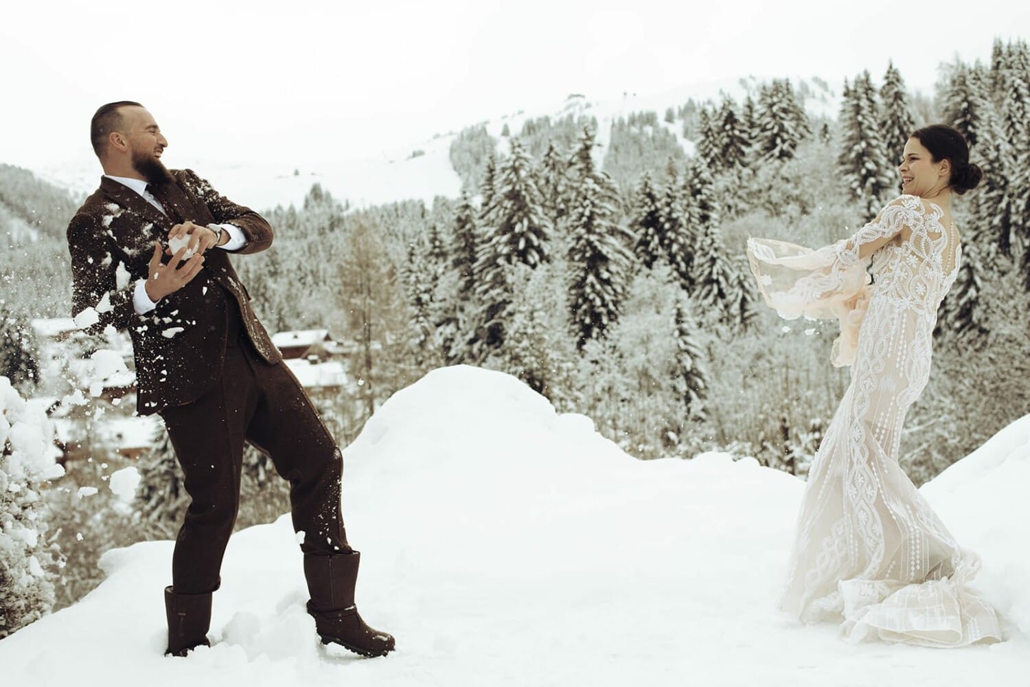 Couple de mariés qui s’amusent dans la neige, devant une forêt enneigée