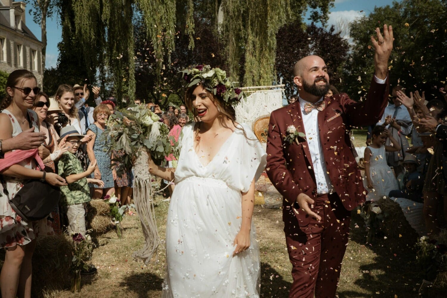 Mariés rayonnants sous une pluie de pétales après la cérémonie, entourés de leurs invités en plein cœur d’un mariage en extérieur.
