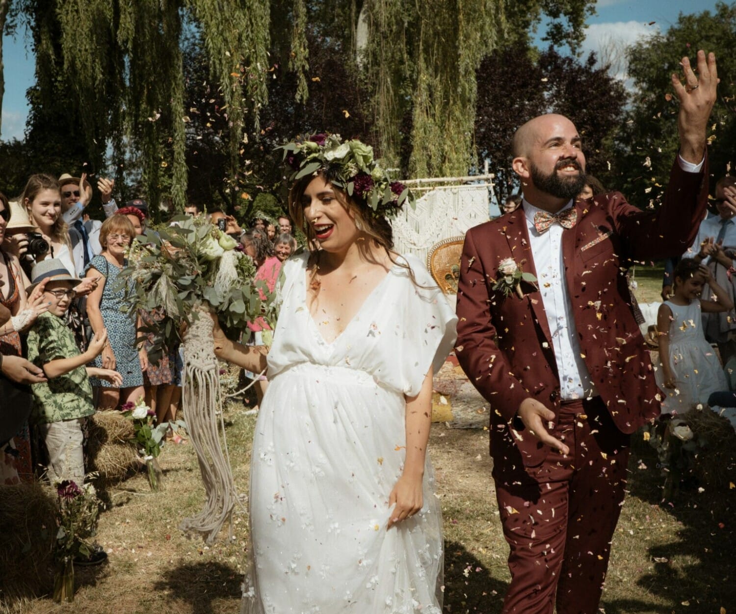 Mariés rayonnants sous une pluie de pétales après la cérémonie, entourés de leurs invités en plein cœur d’un mariage en extérieur.