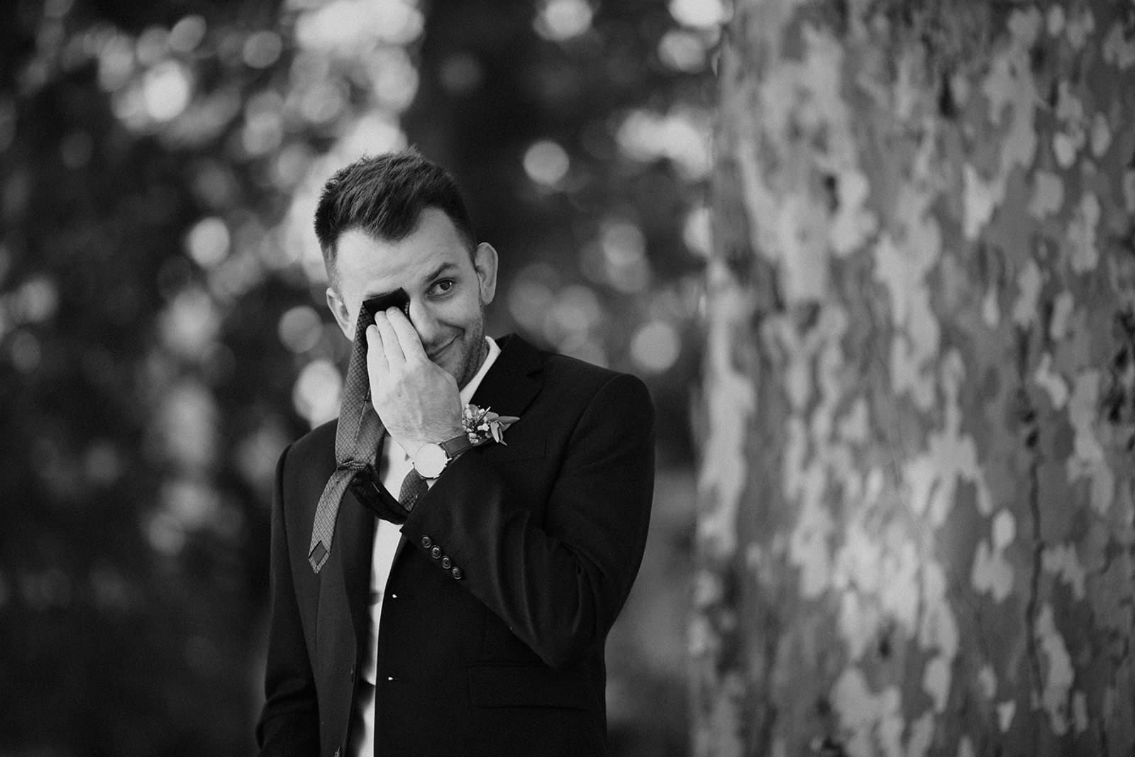 Marié en costume essuyant une larme, saisi dans un moment d’émotion sincère juste avant ou pendant la cérémonie.