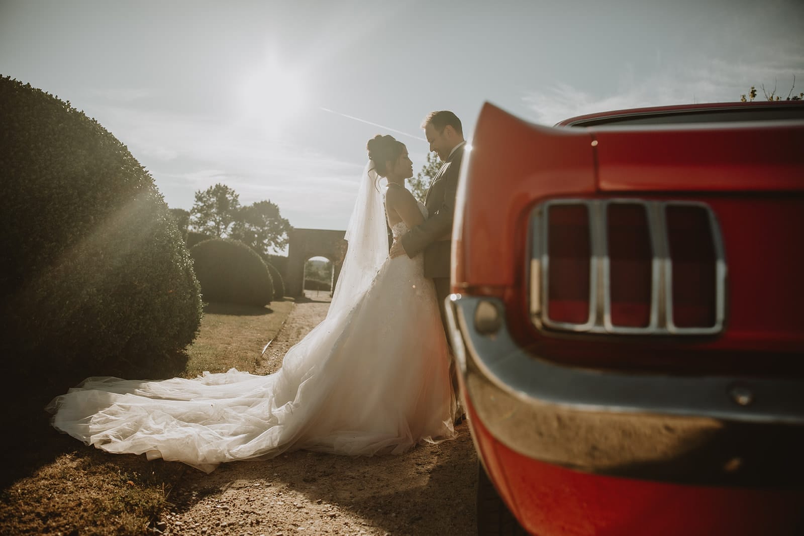 Couple de mariés devant une Mustang rouge au Château de Beauvoir au coucher du soleil